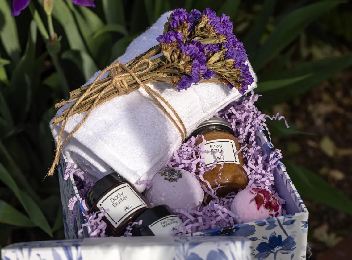 Organic Spa Gift Box for Her Skincare | Natural Beauty Treats Gift for Woman 1 An Organic Spa Gift Box for Her, featuring a wooden box filled with skincare products like a frosted glass jar of face cream, a bottle of body oil, and a lavender bath bomb, all nestled in beige shredded paper. The box is placed on a white linen cloth on a wooden surface, with dried lavender sprigs and a rolled white towel in the background, creating a serene spa vibe.
