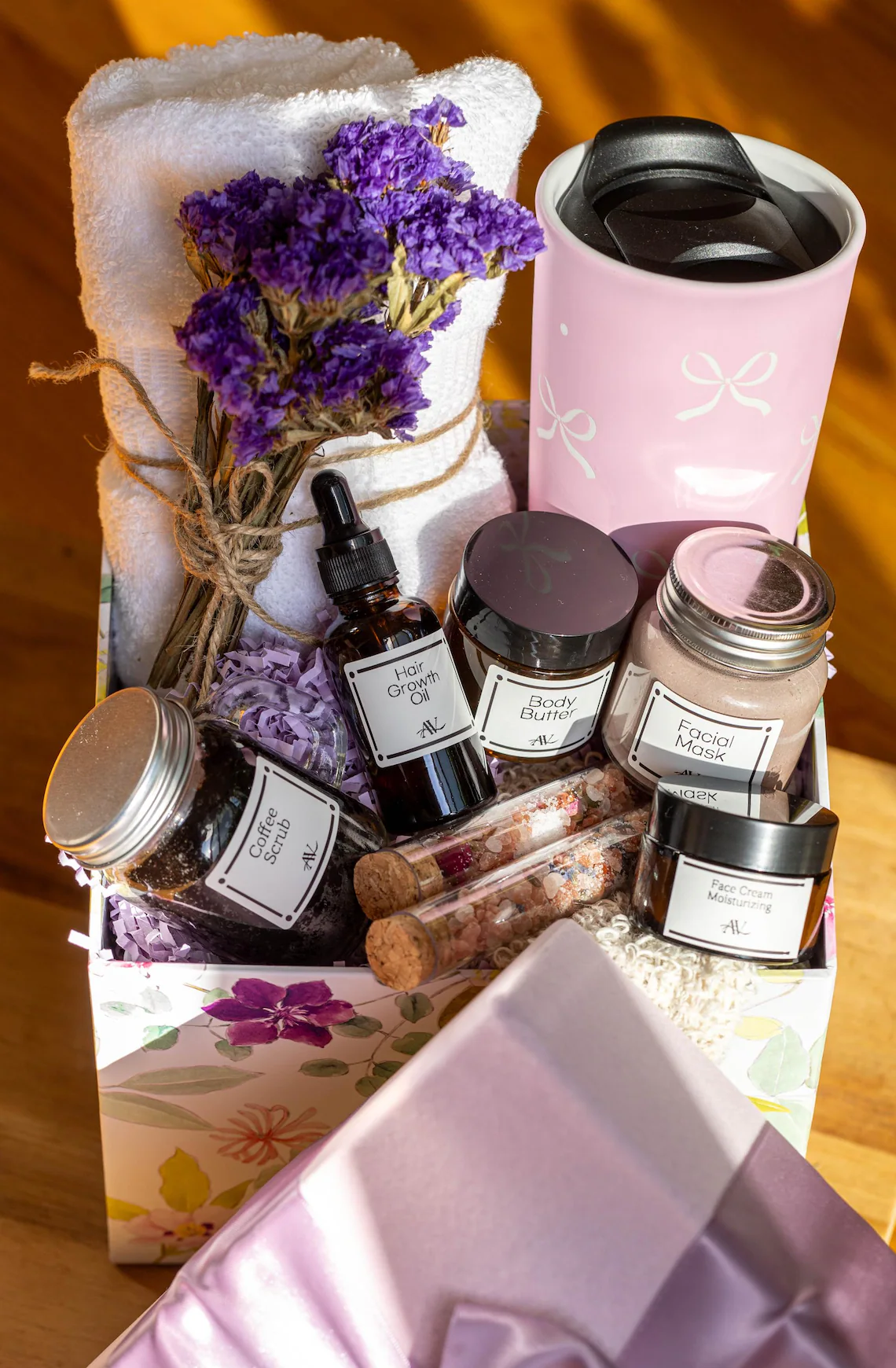 Organic Spa Gift Box for Her Skincare | Natural Beauty Treats Gift Mother's Day 1 An Organic Spa Gift Box for Her, featuring a wooden box filled with skincare products like a frosted glass jar of face cream, a bottle of body oil, and a lavender bath bomb, all nestled in beige shredded paper. The box is placed on a white linen cloth on a wooden surface, with dried lavender sprigs and a rolled white towel in the background, creating a serene spa vibe.