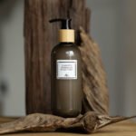Dark green bottle of organic body wash with black pump and minimalist label, placed on rustic wood background